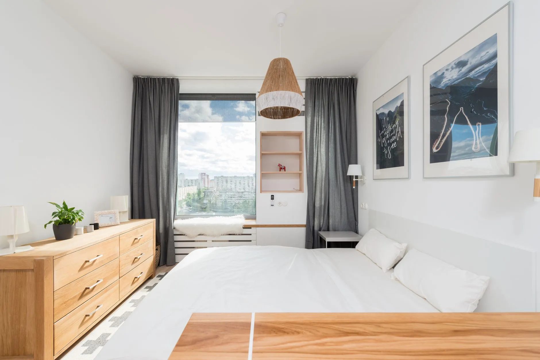 A bright hotel bedroom with a white bed and a window view.
